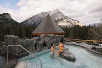 A wooden gazebo with a pool and a fire feature, surrounded by mountains and trees.