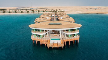 A floating hotel with multiple levels, a central pool, and a view of the surrounding desert and water.