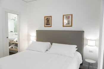 A hotel room with a bed, white curtains, and a window with a metal railing.