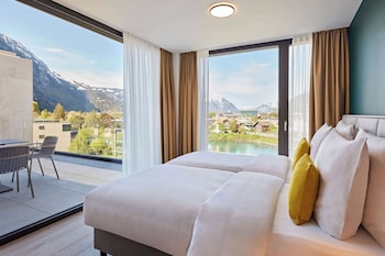 A hotel room with a large bed, a TV, a balcony with a view of mountains and a lake.