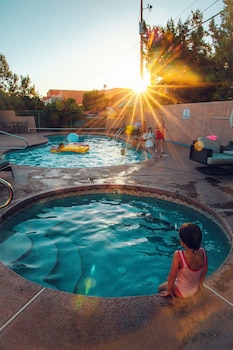 A swimming pool with a child sitting by the edge, surrounded by lounge chairs and a sunlit sky.
