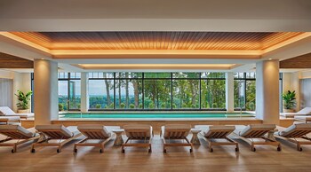 A modern interior with a row of beige sofas and a large window offering a view of trees.