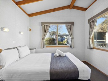 Un dormitorio con cama, ventana con cortinas, vista al exterior y techo con vigas de madera.