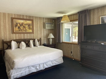 A hotel room with a large bed, a desk, a chair, a TV, and a window with curtains.