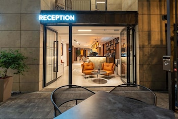 A reception area with a modern interior, including a reception desk, seating area with orange sofas, and a bar with shelves of bottles.