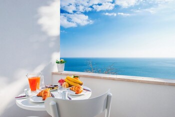A breakfast setup with croissants, bananas, and juice on a balcony overlooking the sea.