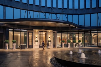 A modern hotel entrance with a curved facade, large windows, and a water feature in the foreground.