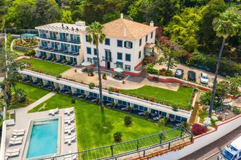 A multi-story hotel with a pool area, outdoor seating, and lush greenery.