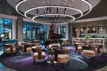 Un espace extérieur aménagé avec un banc en bois, une table où sont disposés des plats, des plantes en pot et une vue sur l’intérieur du bâtiment, visible à travers une porte vitrée.