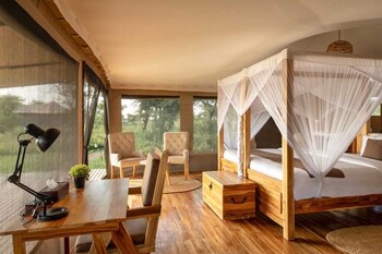 A tented accommodation with a bed, seating area, and a view of the sunset.