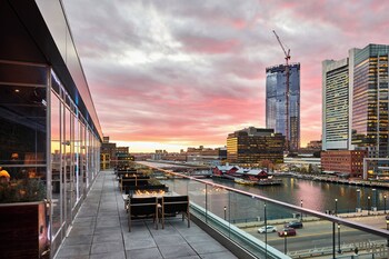 A rooftop terrace with outdoor seating, a pool, and a city skyline in the background.