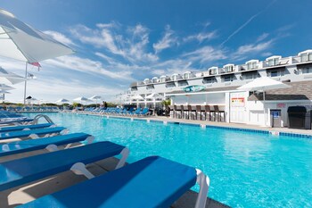 Relax by the pool surrounded by lounge chairs and umbrellas, with a building offering convenient amenities nearby.