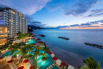 A resort with a large building, a swimming pool, and a view of the sea.