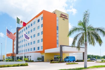 A modern hotel entrance with a well-lit facade, a clear sign for Hampton Inn & Suites, and a paved driveway leading to the entrance.