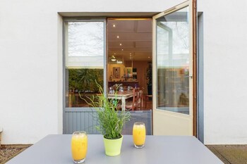 Una puerta abierta que da a un comedor con una mesa dispuesta para dos personas, una planta en maceta y dos vasos de zumo de naranja sobre la mesa.