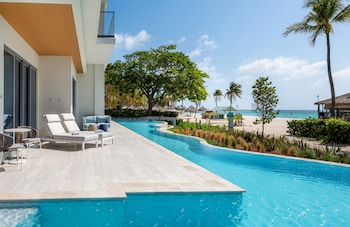 An aerial view of a beach resort with a swimming pool, palm trees, and beach umbrellas.