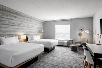 A modern hotel lobby with a central dining area, sofas, and a seating area with a view of the cityscape.