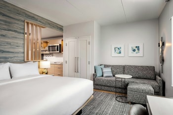A modern hotel lobby with a central dining area, sofas, and a seating area with a view of the cityscape.