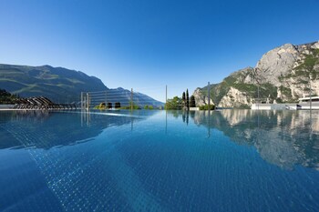 A clear blue pool with a mountain backdrop, a wooden deck with lounge chairs, and a rocky cliff.