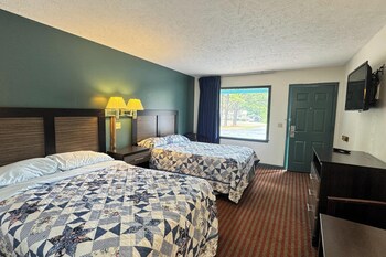 A hotel room with two beds, each with a floral-patterned quilt, a nightstand with a lamp, and a plain wall.