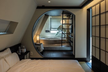 A bedroom with a large bed, a view of a bathroom with a bathtub, and a sliding door leading to a balcony.