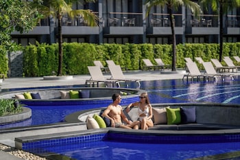 A swimming pool with multiple lanes, surrounded by palm trees and lounge chairs, with a building in the background.
