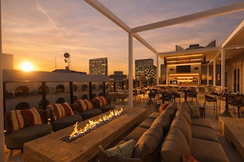 Un bar situé sur un toit, doté d’un foyer, de sièges et offrant une vue panoramique sur la ville.