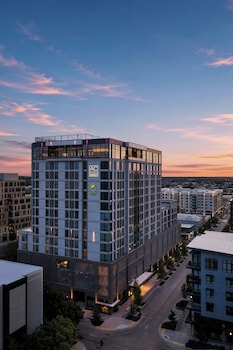 A modern hotel building with a prominent logo, large windows, and a well-lit entrance area.