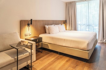 A large bed with white linens, a bedside table with a lamp, and a wooden panel wall.