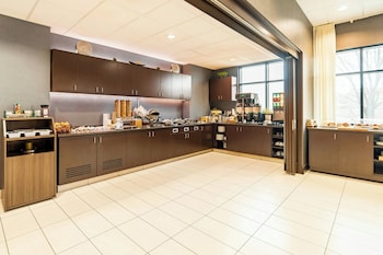 A modern hotel lobby with a long corridor, a large abstract painting, a potted plant, and a glass door entrance.