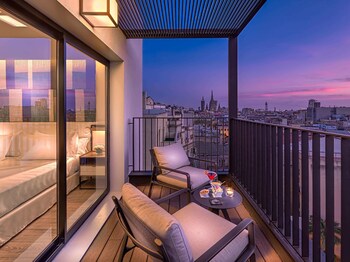 En balkon med udsigt over byen i skumringen, med en sofa, stole og et lille bord med snacks og en drik.