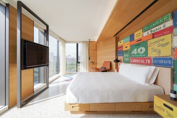 Habitación de hotel con una cama grande, un escritorio y vistas a la ciudad a través de cortinas translúcidas.