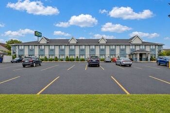 A hotel with a parking lot, a dumpster, and a sign for a nearby restaurant.