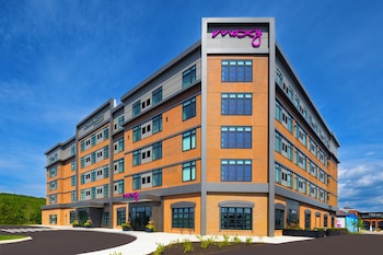 A multi-story hotel with 'Resilience Inn' and 'Mozy Hotels' signage, featuring a modern brick facade and multiple ground-level retail spaces.