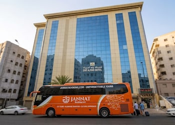 Un moderno edificio de hotel con fachada de vidrio reflectante, una palmera delantera y el nombre 'ZAD AJYAD HOTEL' exhibido al frente.