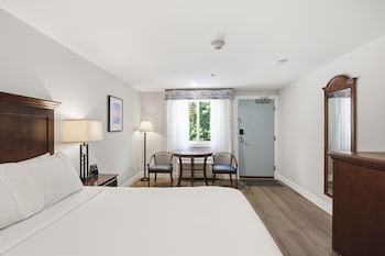 Un dormitorio con cama, mesitas de noche, un sofá, una ventana con cortinas y obras de arte en las paredes.