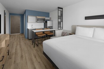 A hotel room with a bed, a desk with a chair, a microwave, and a refrigerator.
