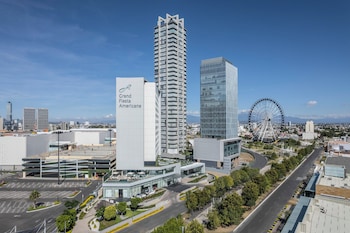 A modern hotel room with a large dining table, comfortable seating, a flat-screen TV, and a city view through large windows.