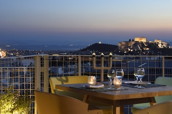 Una mesa con copas de vino y una menorá, con vistas a un paisaje urbano y ruinas antiguas al anochecer.