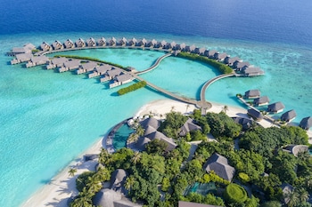 Vista aérea de un resort con bungalows sobre el agua, una piscina central y una zona de playa.