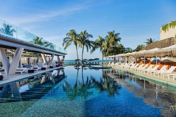 Relax by the infinity pool overlooking the ocean, surrounded by palm trees and lush greenery.