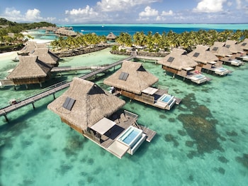 An overwater bungalows with thatched roofs, clear turquoise water, and palm trees.