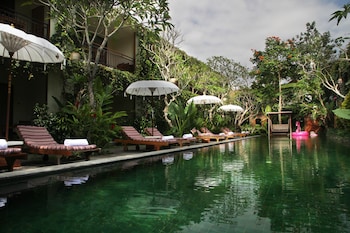 Zona de piscina con sillones de descanso y sombrillas, rodeada de exuberante vegetación.