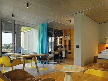 Une chambre moderne avec une grande fenêtre, une plante en pot, une chaise bleue et un journal.
