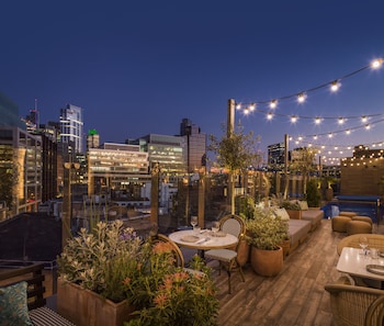 A rooftop pool area with string lights, a seating area, and a view of the cityscape at night.