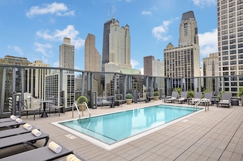 Una piscina en la azotea con sillas de descanso y un horizonte urbano de fondo.