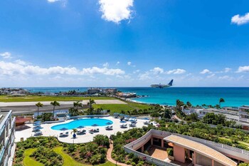 Une plage à l’eau turquoise et limpide, une rive sablonneuse et un hôtel doté de nombreux balcons donnant sur la mer.