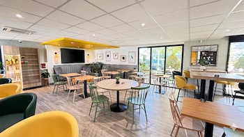 Habitació d'hotel moderna amb un llit ben fet, un calefactor verd fixat a la paret i un moble d'emmagatzematge verd amb roba penjada.