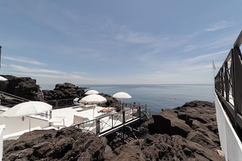 Eine felsige Küstenlandschaft mit weißen Sonnenschirmen und Liegestühlen auf einer Terrasse mit Blick aufs Meer.