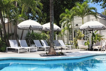A pool area with lounge chairs and umbrellas, surrounded by palm trees and a building with a white facade.